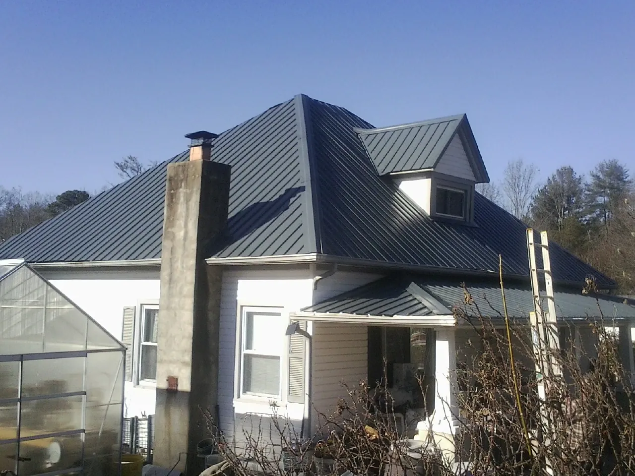 Dark blue standing seam metal roof on a white farmhouse with dormer — Slate & Tile Roof Repair by Roofing Brothers in Pigeon Forge