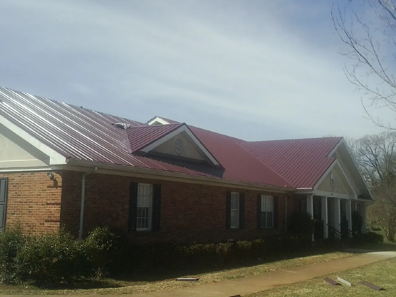 Red metal roof with gabled entries on a long brick building, from a Hail Damage Roof Repair job in Pigeon Forge