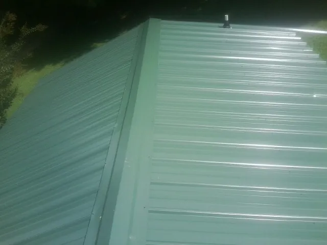 New green metal panels meeting at the ridge of a roof — Flat Roof Repair work by our crew in Pigeon Forge