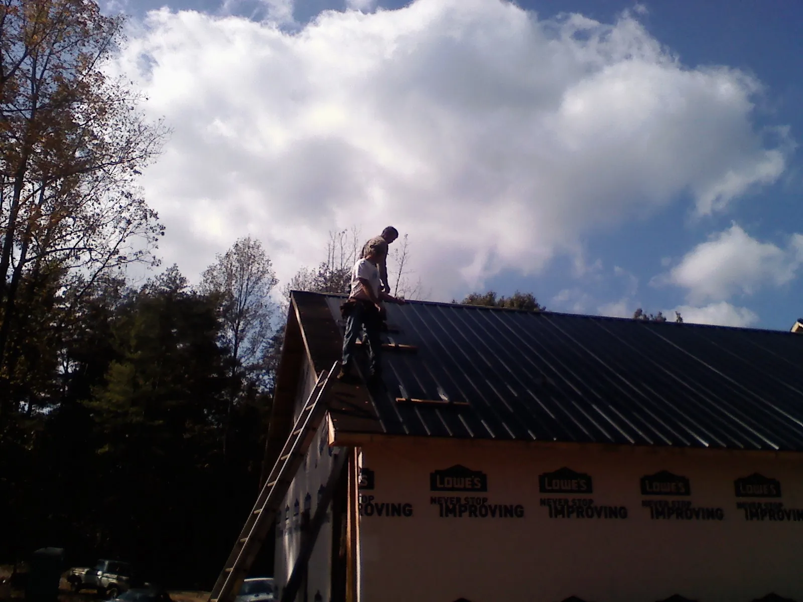 Roofer fastening dark metal panels high against a cloudy sky, from a Roof Inspection job in Pigeon Forge