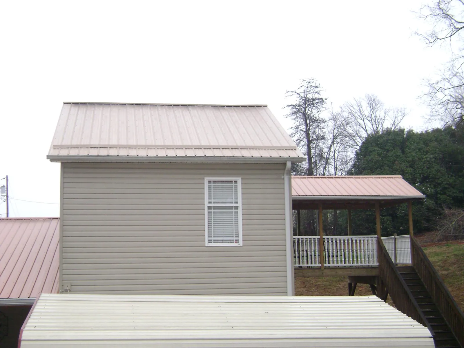 Tan metal roofs on a two story addition and attached porch, from a Roof Replacement job in Pigeon Forge